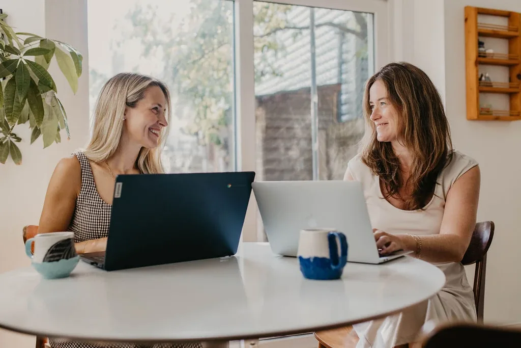Liz and Nancy smiling while working together at a table